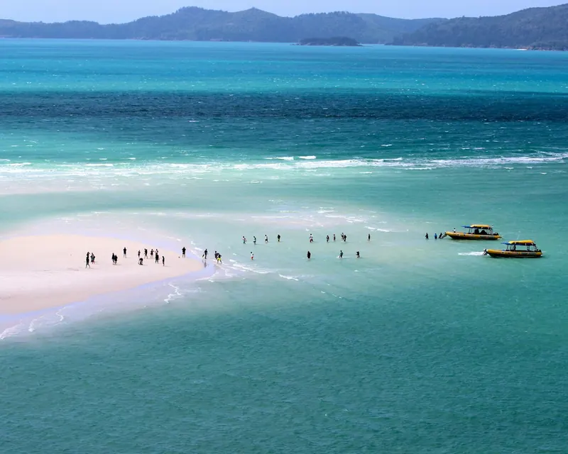 People walking on a Whitehaven sandbar with two tour boats at anchor